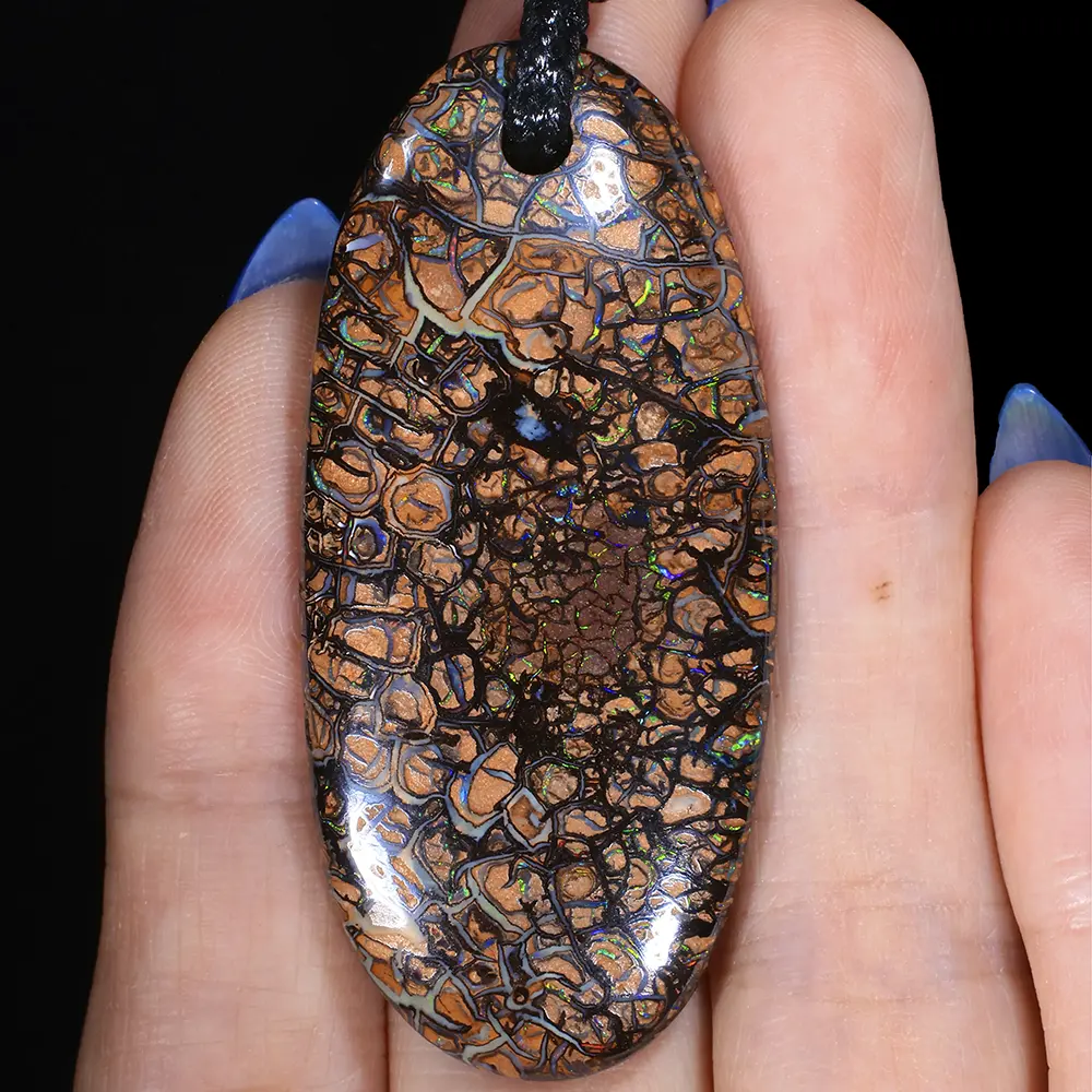 Boulder opal pendant with koroit pattern showing green and blue flashes, held in hand