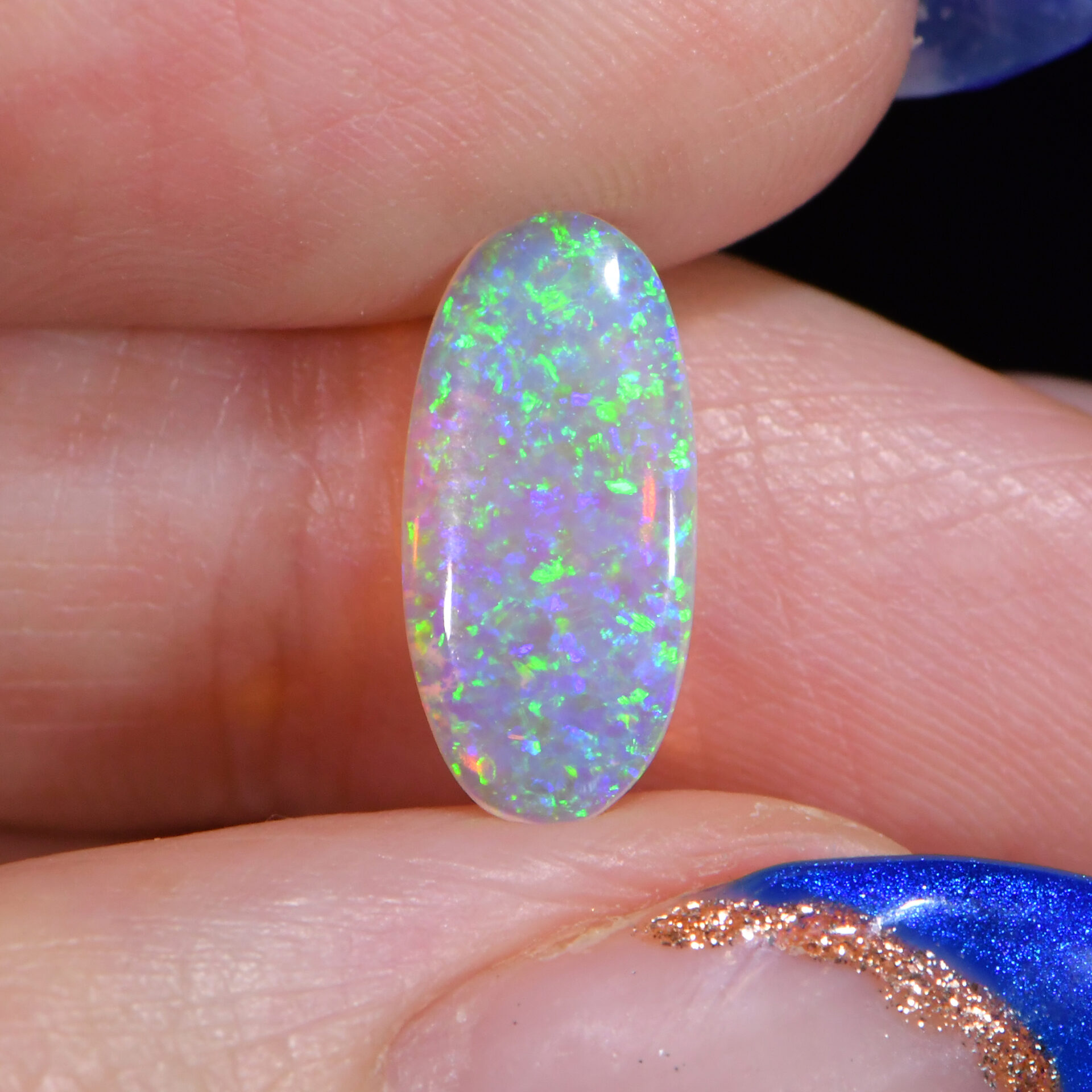 Green blue crystal boulder opal 1.07 ct close view in fingers showing fine green blue sparkle across the face.
