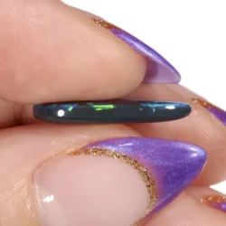 Edge-on view of a 2.84ct natural black opal teardrop held between fingers, showing the thin profile and green and blue colour play along the polished surface, Lightning Ridge Australia