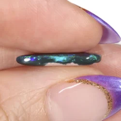 Profile view of a 2.84ct natural black opal teardrop cabochon held between fingers, showing the slim polished edge and green and blue colour flash, Lightning Ridge Australia