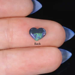Back view of a 0.54ct natural black opal heart resting on a finger, showing green and violet colour play through a dark grey body tone, Lightning Ridge Australia