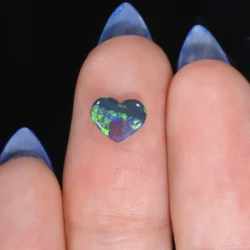 0.54ct solid black opal heart resting on a fingertip, displaying vivid green and violet play-of-colour against a dark body tone, Lightning Ridge Australia