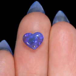 0.8ct natural untreated black crystal opal carved into a heart shape, resting on a fingertip, showing electric blue and purple colour flash, Lightning Ridge Australia