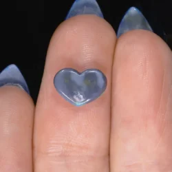 0.96ct natural black opal heart resting on a fingertip, showing subtle green and blue colour flash beneath a grey semi-translucent body, Lightning Ridge Australia
