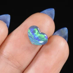 0.96ct untreated black opal heart resting in a palm, showing bright green and blue colour play across a dark semi-translucent body, Lightning Ridge Australia