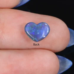 Back view of a 1.11ct solid black crystal opal heart cabochon resting on fingers, showing green and blue colour play across the surface, Lightning Ridge Australia