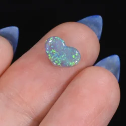 1.19ct solid dark opal heart resting on a finger at an angle, displaying bright green and blue colour flash across a semi-translucent body, Lightning Ridge Australia
