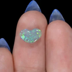 1.19ct untreated natural dark opal heart resting on a fingertip, showing vivid green and teal play-of-colour across a light crystal body, Lightning Ridge Australia