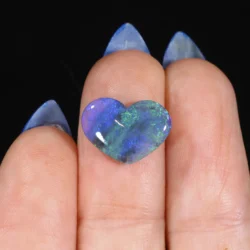 1.99ct natural black opal heart resting across two fingertips, displaying blue, green and violet play-of-colour against a dark semi-translucent body, Lightning Ridge Australia