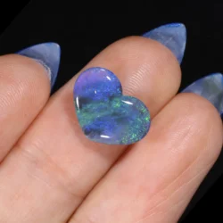 1.99ct untreated black opal heart resting in a palm, showing sweeping green and blue colour play with violet accents across a dark body tone, Lightning Ridge Australia