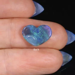 Back view of a 1.99ct natural black opal heart resting across fingers, showing green and blue colour play through a semi-translucent body, Lightning Ridge Australia