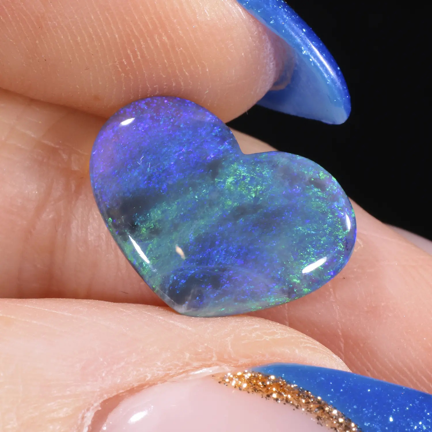 1.99ct solid black opal heart held between fingers in close-up, displaying vivid violet, blue and green play-of-colour across a dark semi-translucent body, Lightning Ridge Australia