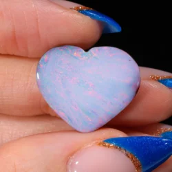 14.75ct untreated boulder opal heart held in hand, exhibiting delicate pastel pink, red and green colour flashes across a soft blue-white body, Winton Queensland Australia