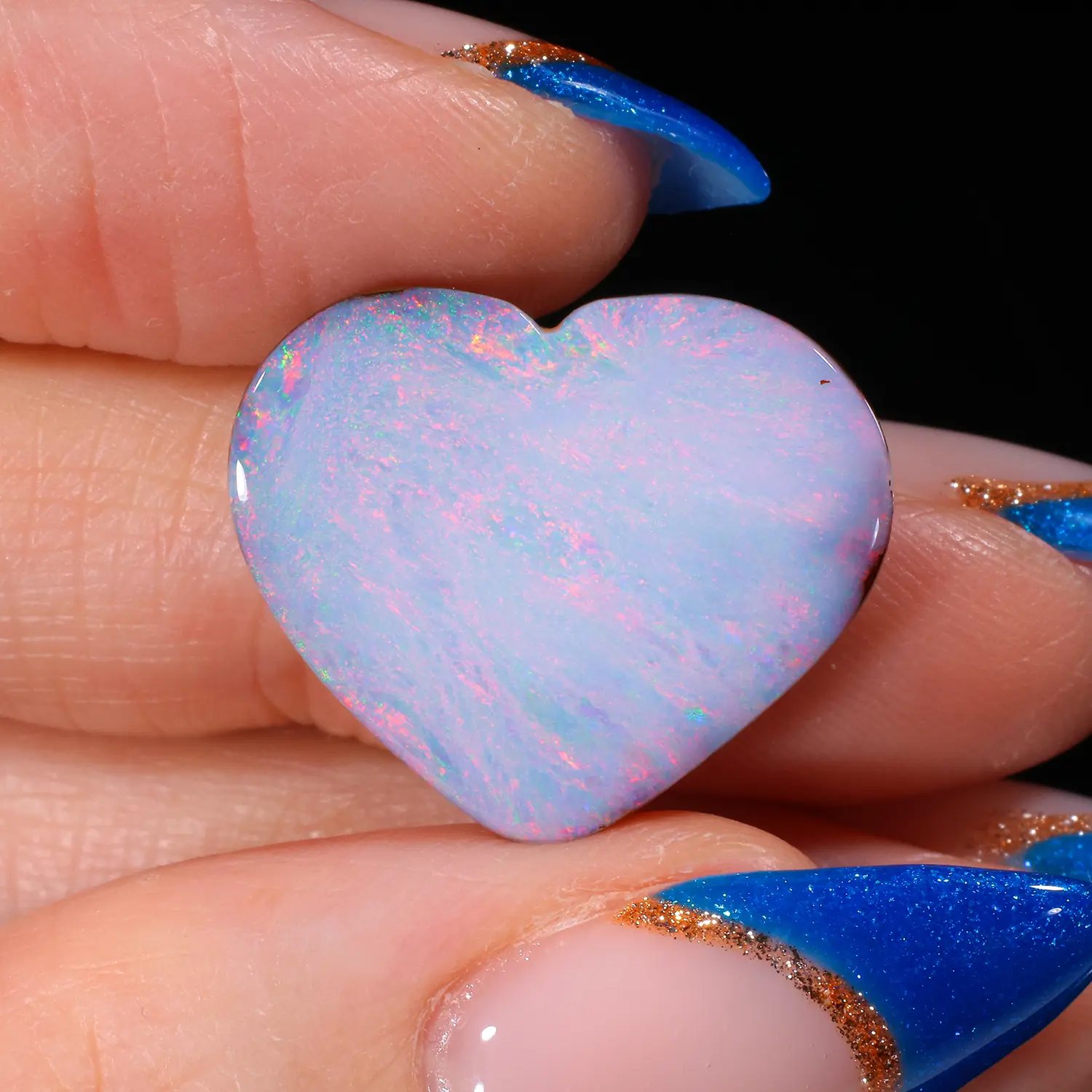 14.75ct untreated boulder opal heart held in hand, exhibiting delicate pastel pink, red and green colour flashes across a soft blue-white body, Winton Queensland Australia