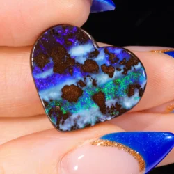 16.5ct natural boulder opal heart cabochon held between fingers, showing vivid blue, violet and green play-of-colour against dark ironstone matrix, Winton Queensland Australia