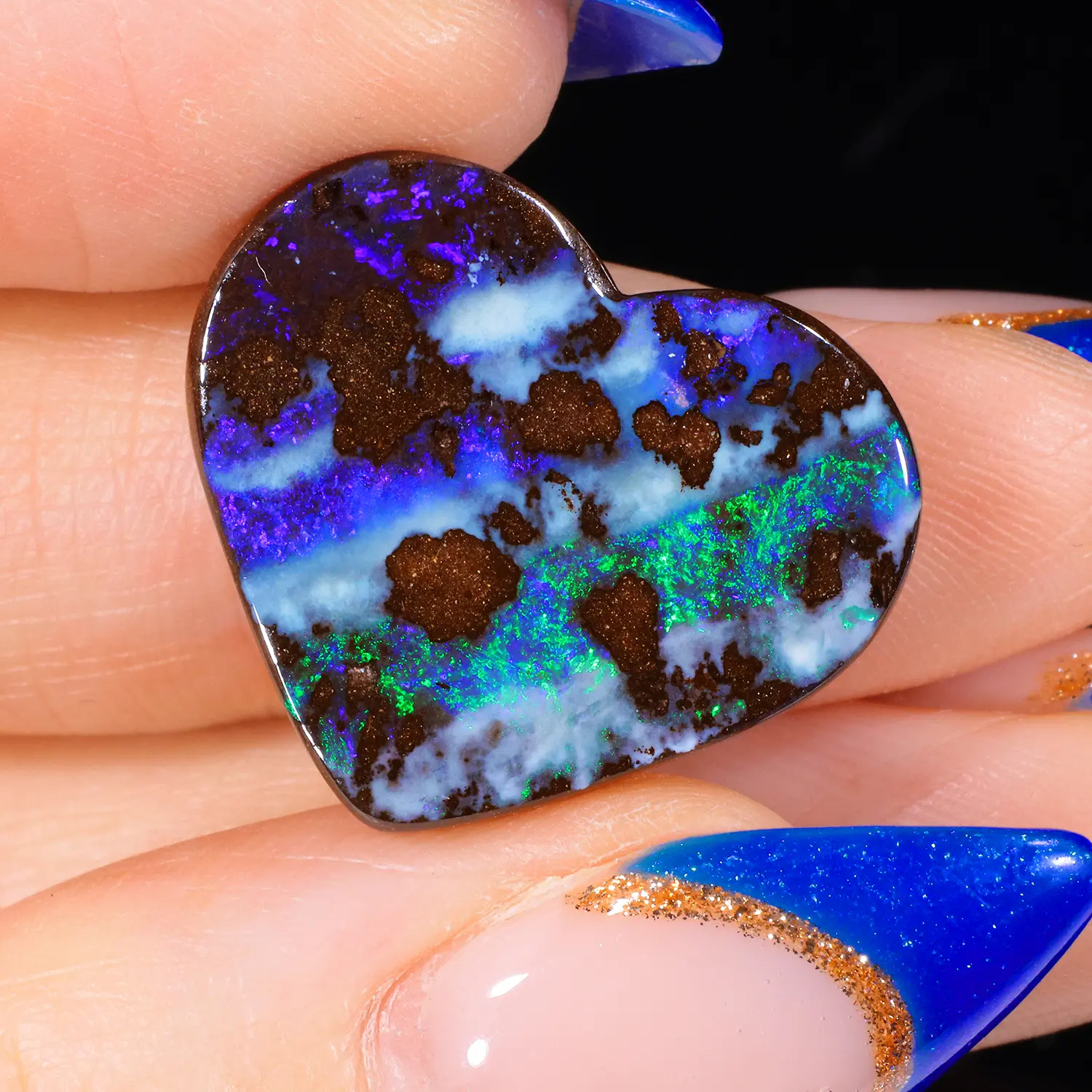16.5ct natural boulder opal heart cabochon held between fingers, showing vivid blue, violet and green play-of-colour against dark ironstone matrix, Winton Queensland Australia