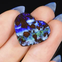 16.5ct solid boulder opal carved into a heart shape, held in a palm, displaying electric blue, purple and green fire with natural ironstone matrix, Winton Queensland Australia