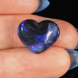 5.26ct natural solid black opal heart resting in a palm, displaying deep electric blue play-of-colour with violet and white streaks against a dark black body tone, Lightning Ridge Australia