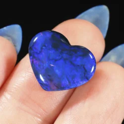 5.26ct natural black opal heart held against fingers, displaying deep royal blue and purple play-of-colour across a polished dark body, Lightning Ridge Australia