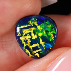 Close up of black opal showing yellow green fire in full Chinese writing pattern held between fingers