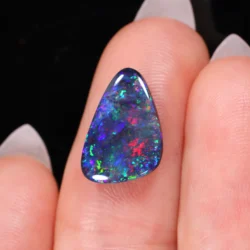 Close up of freeform black opal showing red green blue yellow orange and cyan fire on fingertip-xx1873