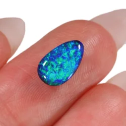 Close-up of solid black opal teardrop showing intense turquoise blue and green fire, held on fingertip xx1871