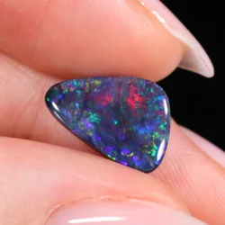 Triangular freeform black opal with mixed color fire held in fingers-xx1873