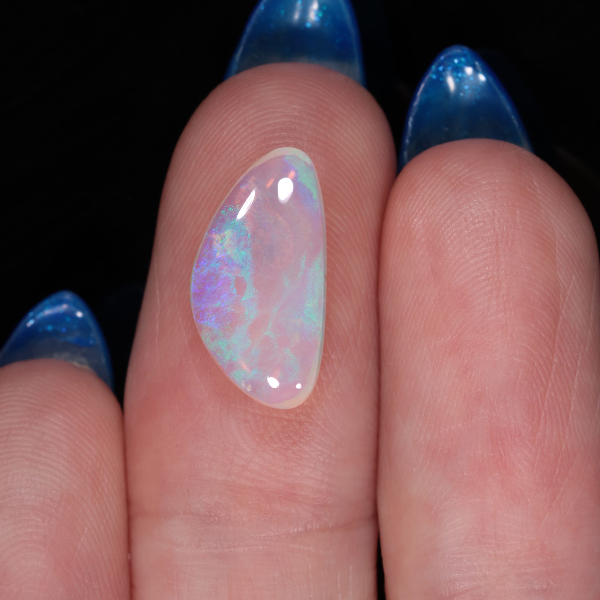 Crystal boulder opal 22.6 ct freeform pipe opal on fingers to show size with green blue fire and clear body tone.