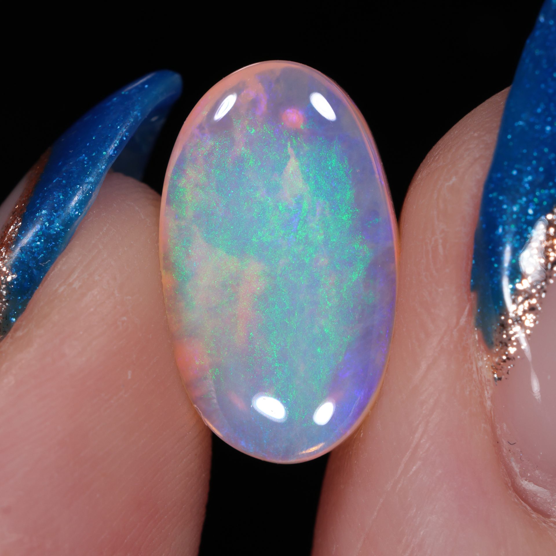 Natural crystal boulder opal 38.3 ct oval pipe opal held in fingers showing soft blue green color and clear body.