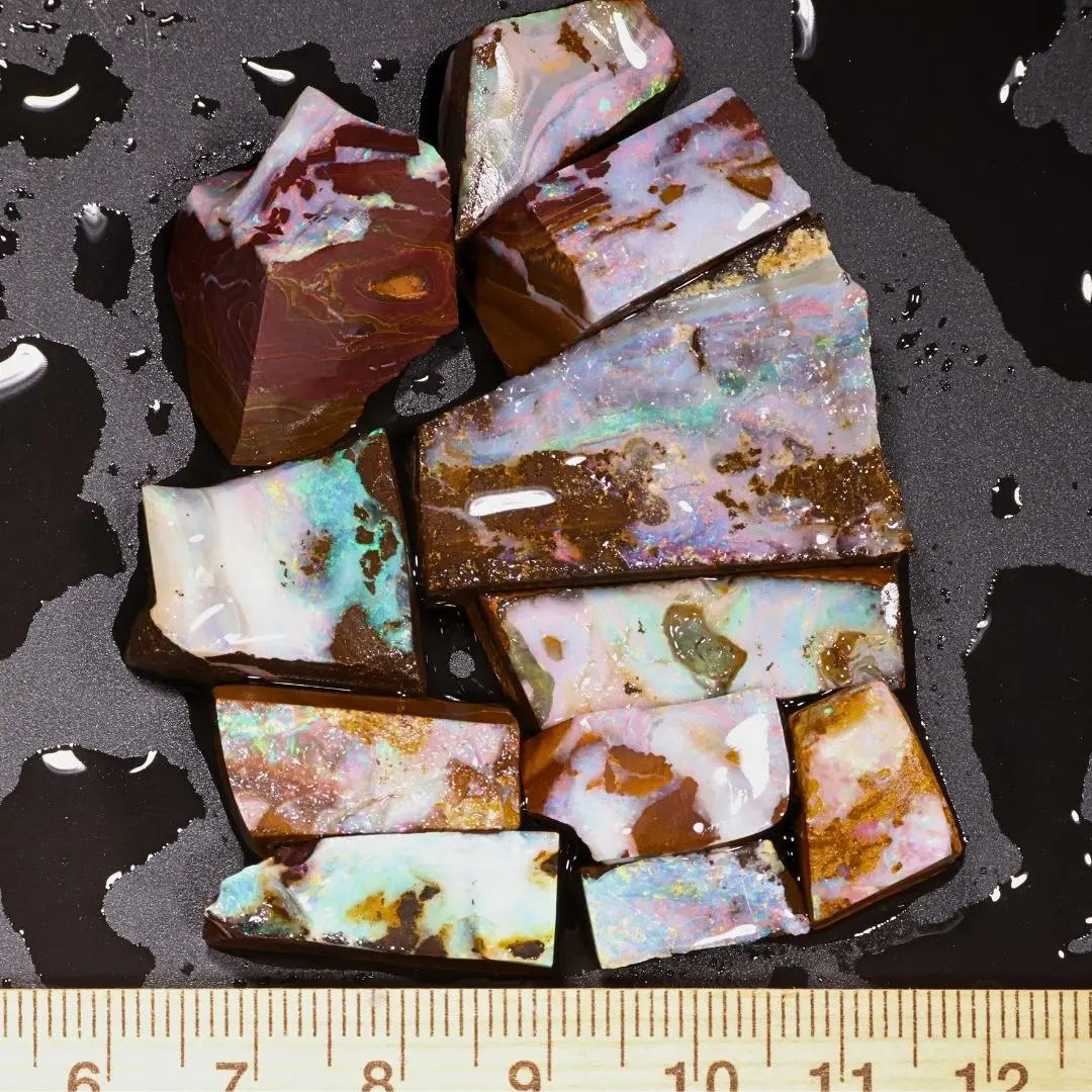 50g parcel of 11 Rainbow Matrix Boulder Opal rubs from Winton Australia showing green pink and blue color in ironstone beside a ruler