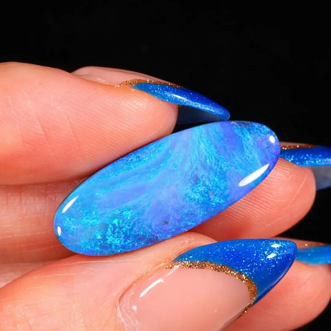 Australian black opal from Mulga Field featuring flowing ocean blue, turquoise green and violet play of color in a close up hand view.