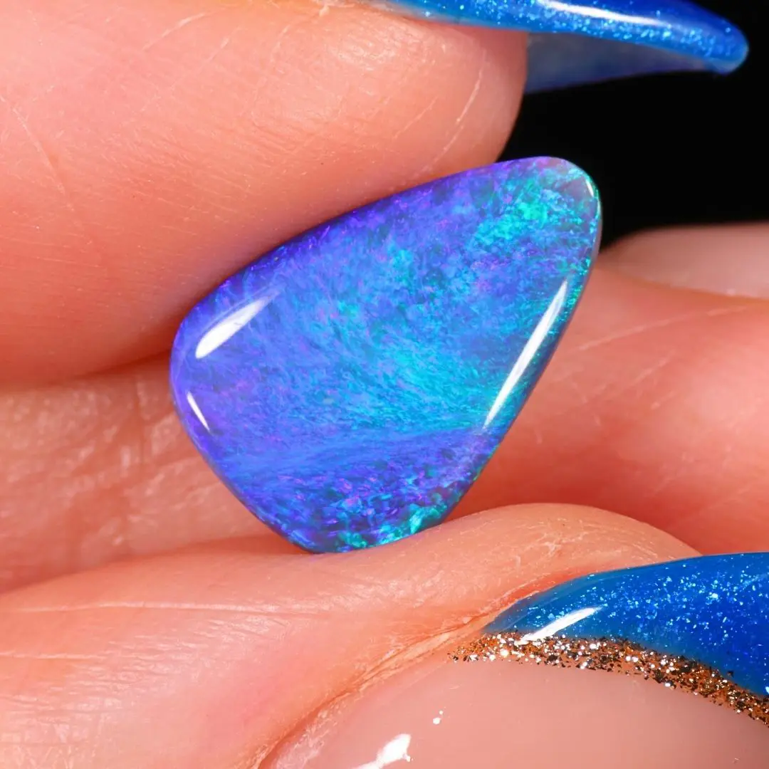 Australian black opal from Mulga Field with bright ocean blue, turquoise green and violet flashes shown in a close up hand view.