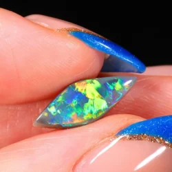 Australian dark opal from Allawah Field displaying brilliant electric green, golden yellow and blue broad flashes in a close up hand view.