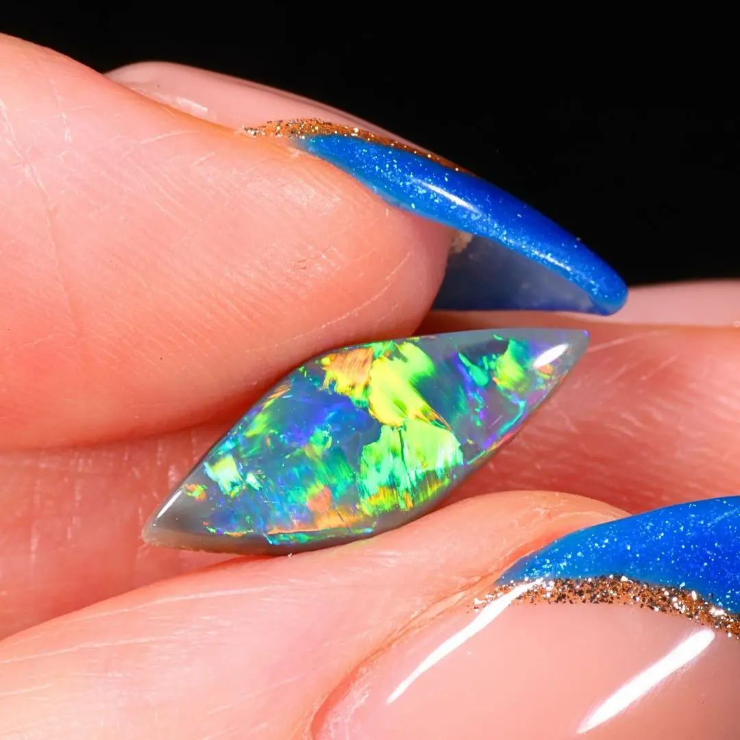 Australian dark opal from Allawah Field displaying brilliant electric green, golden yellow and blue broad flashes in a close up hand view.