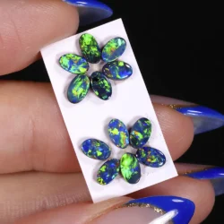 Australian opal doublet parcel of 12 oval stones showing bright neon green, blue and orange color from an angled hand held view.