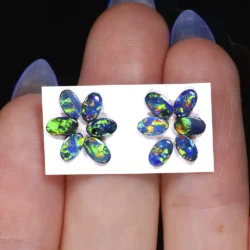 Twelve small 5x3mm Australian opal doublets arranged in two groups of six on a white card and held on fingers for size comparison.