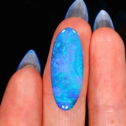 Natural Lightning Ridge black opal 11.76ct elongated oval gemstone showing vibrant ocean blue and green colors on finger for scale.
