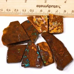 Full parcel of 8 natural Winton Boulder Opal ringstone rubs weighing 72 grams, showing earthy brown ironstone matrix with blue, green and red opal flashes beside a ruler.